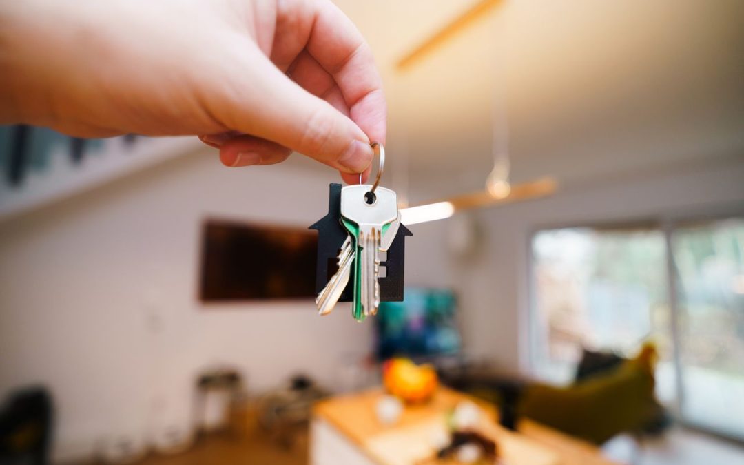 Landlord holding house keys on a house-shaped keychain inside a bright, well-kept rental home, showing the habits of a good landlord